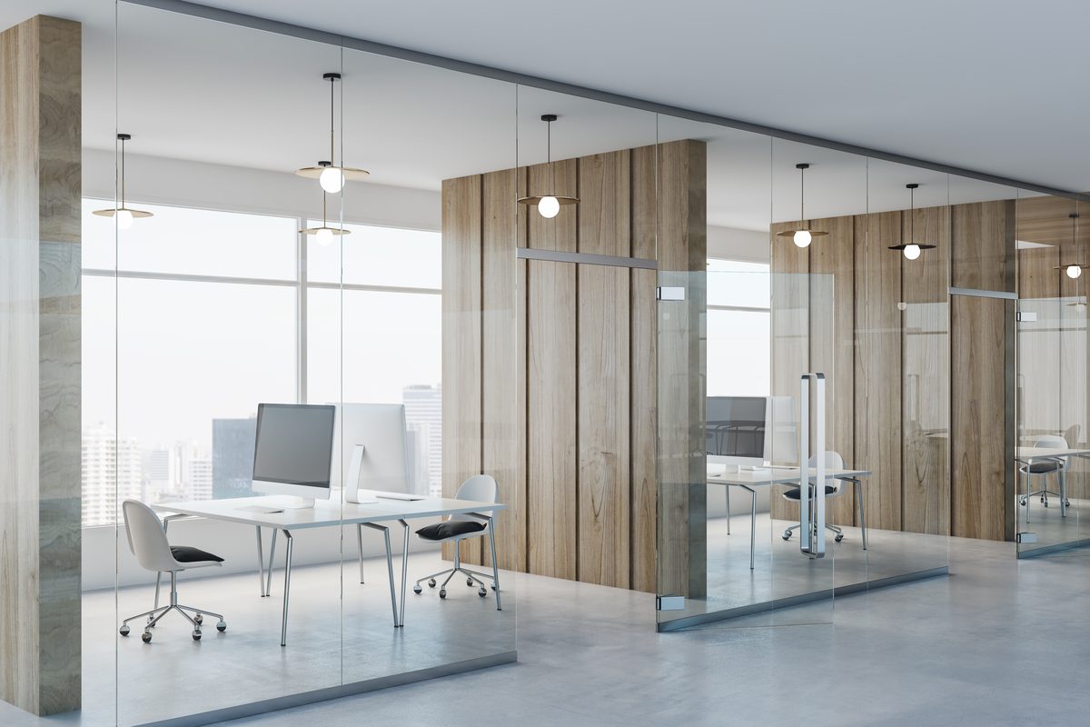 Glass-walled private offices with timber panelling, white desks with computer screens and globe pendant lights